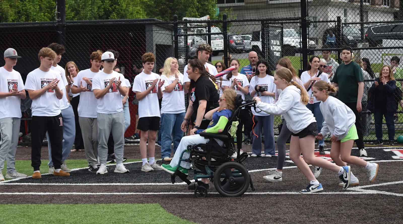 students push a student in a wheelchair up the first base line